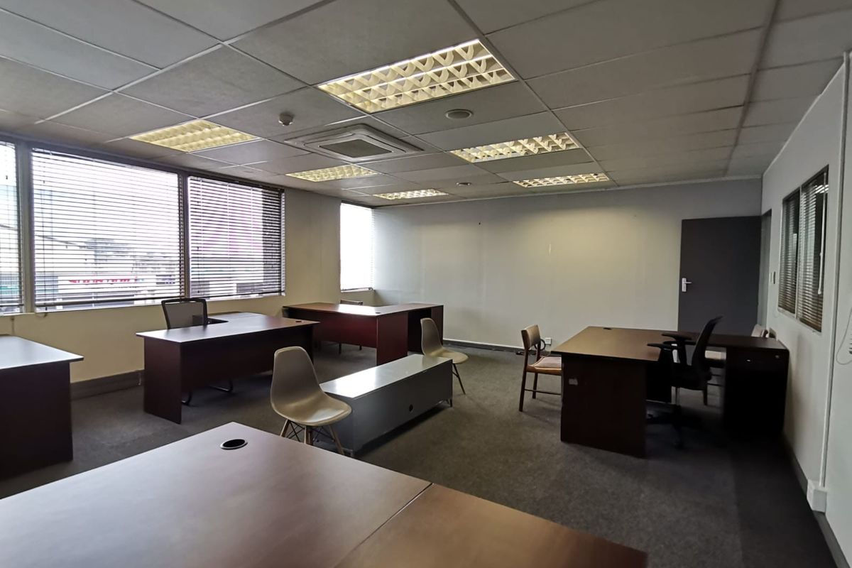 A functional office space featuring a suspended ceiling with recessed lighting, carpeted flooring, and large windows with venetian blinds.