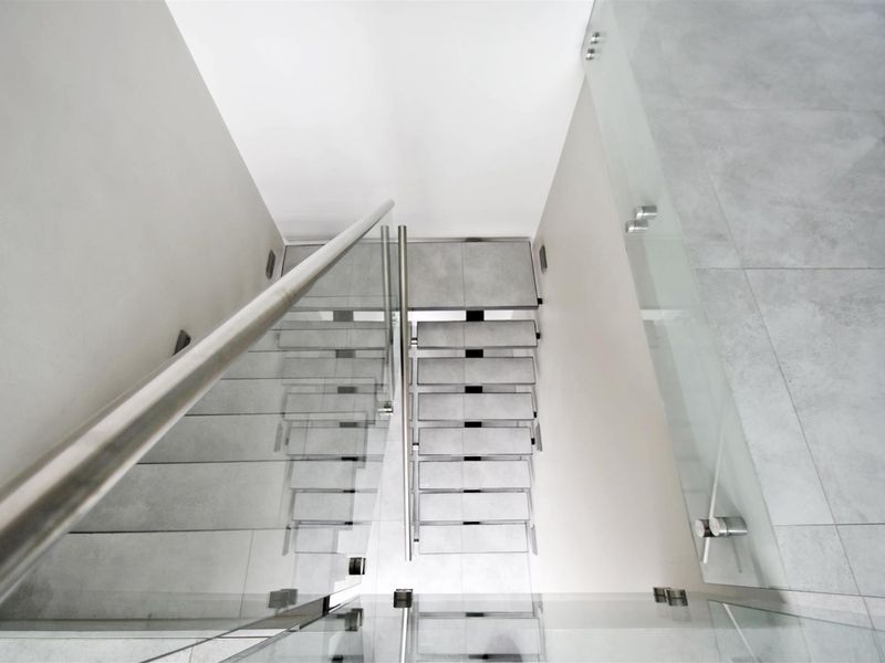 A modern staircase featuring tiled steps, a sleek glass balustrade, and a stainless steel handrail, showcasing a clean and contemporary architectural design.