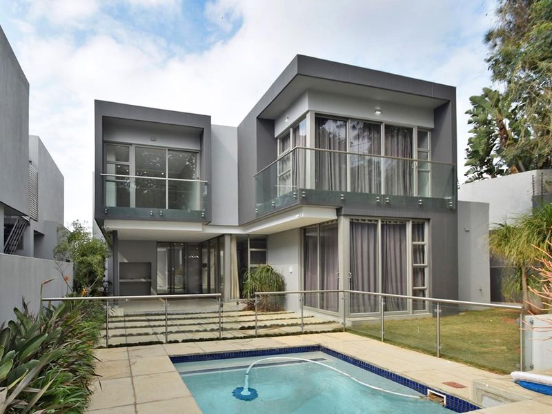 Modern double-storey residence featuring a rear patio, swimming pool, glass balustrades, and expansive sliding doors opening to the garden.