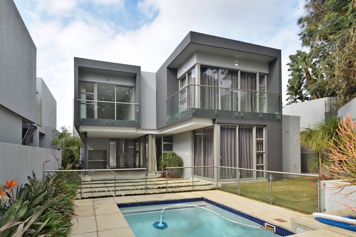 Modern double-storey residence featuring a rear patio, swimming pool, glass balustrades, and expansive sliding doors opening to the garden.