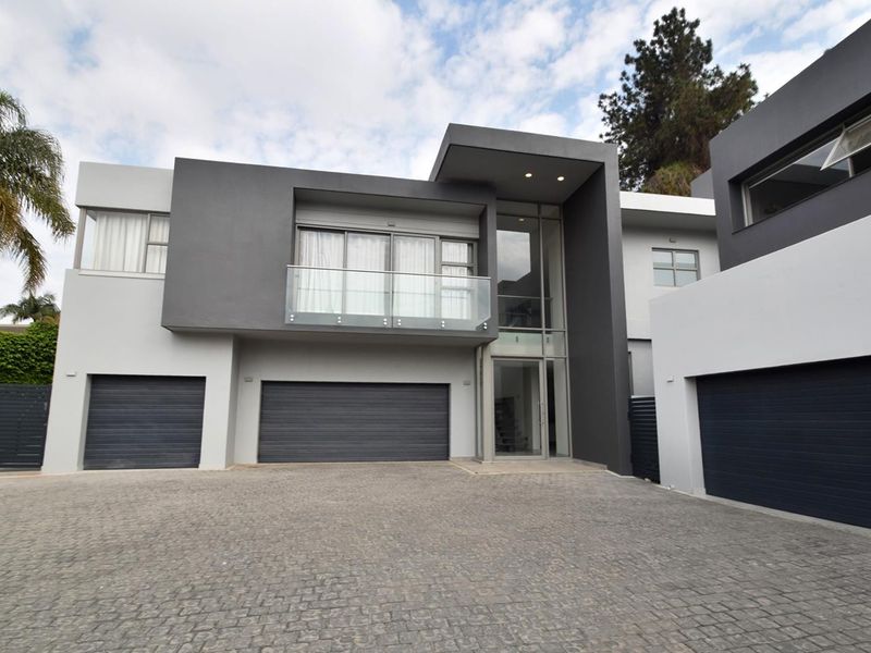 Modern double-story residence featuring a contemporary grey and white facade, multiple garage bays, and a glass-fronted balcony.