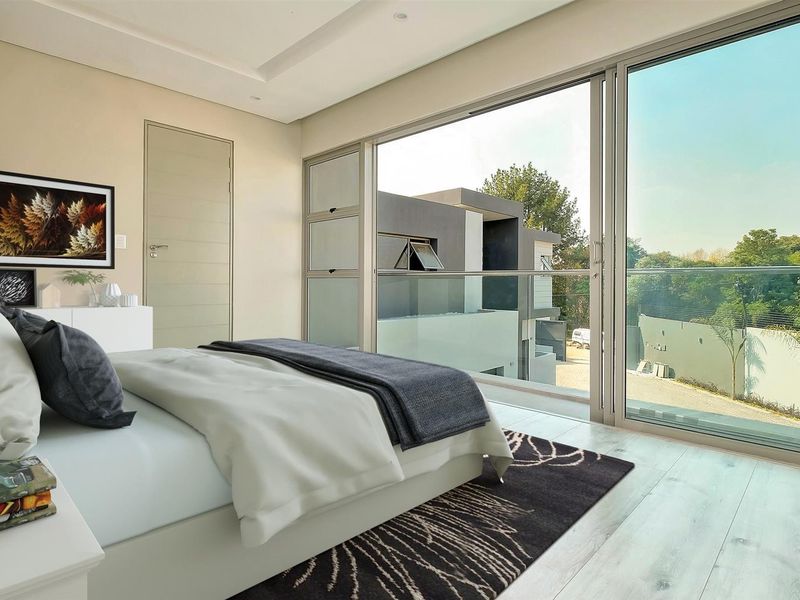 Modern bedroom featuring light laminate flooring, recessed ceiling lighting, and large sliding glass doors opening onto a balcony with a glass balustrade.