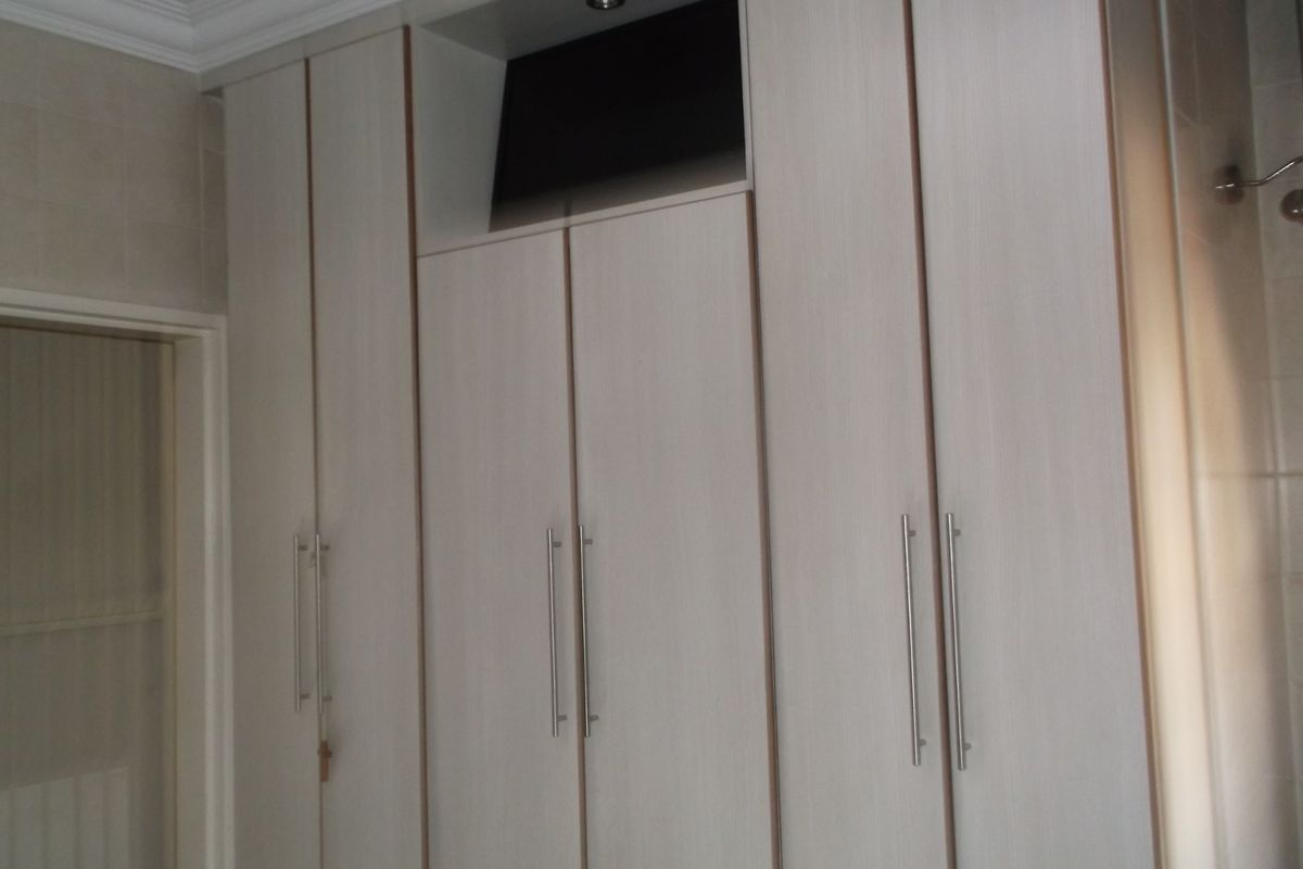 A bedroom featuring floor-to-ceiling built-in cupboards with modern handles and a recessed downlight.