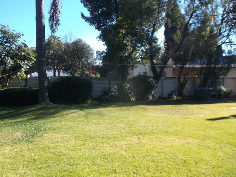A spacious, well-maintained garden featuring a large lawn area, mature trees, and a secure boundary wall.
