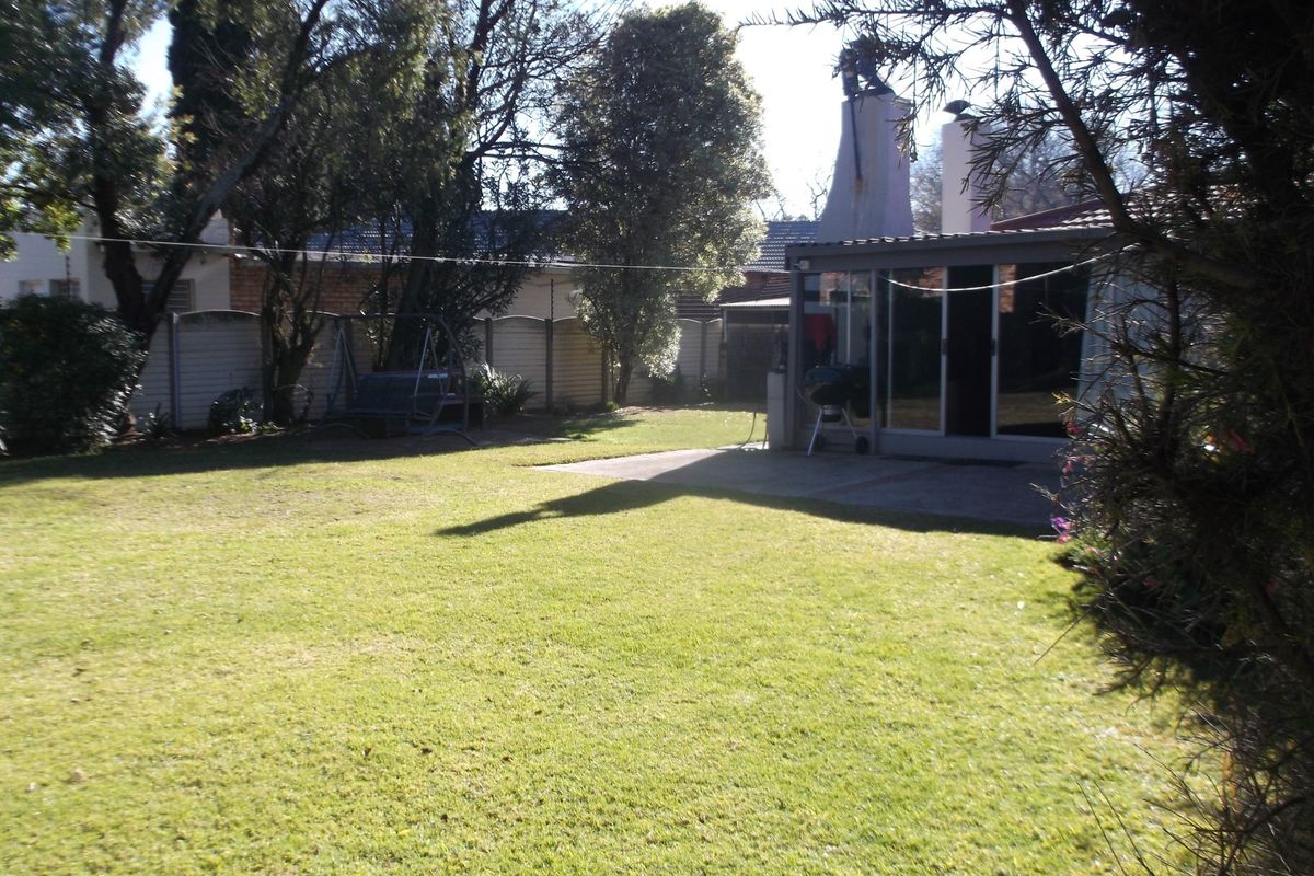 A spacious rear garden featuring a well-maintained lawn, a concrete patio area, and an outdoor fireplace chimney attached to the rear of the house.