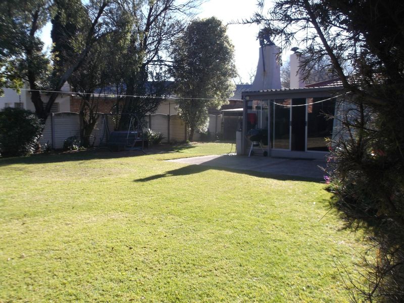 A spacious rear garden featuring a well-maintained lawn, a concrete patio area, and an outdoor fireplace chimney attached to the rear of the house.