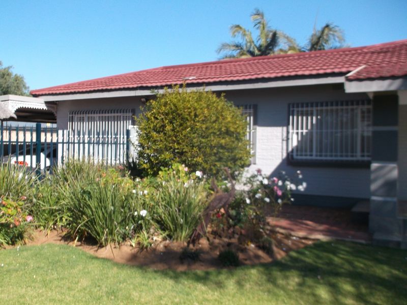 Front view of a single-story house featuring a tiled roof, security bars on windows, and a well-maintained front garden with a paved walkway.