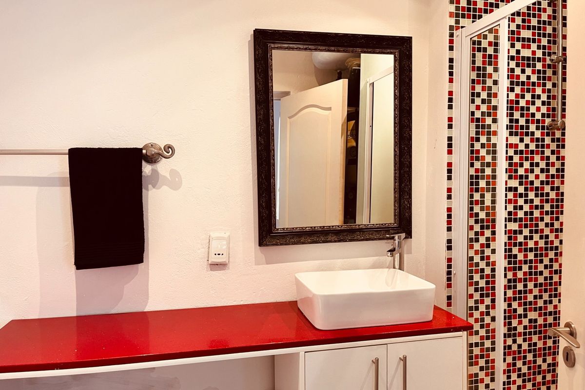 Bathroom featuring a vessel sink on a red vanity countertop, a wall mirror, and a shower enclosure with decorative mosaic tiling.