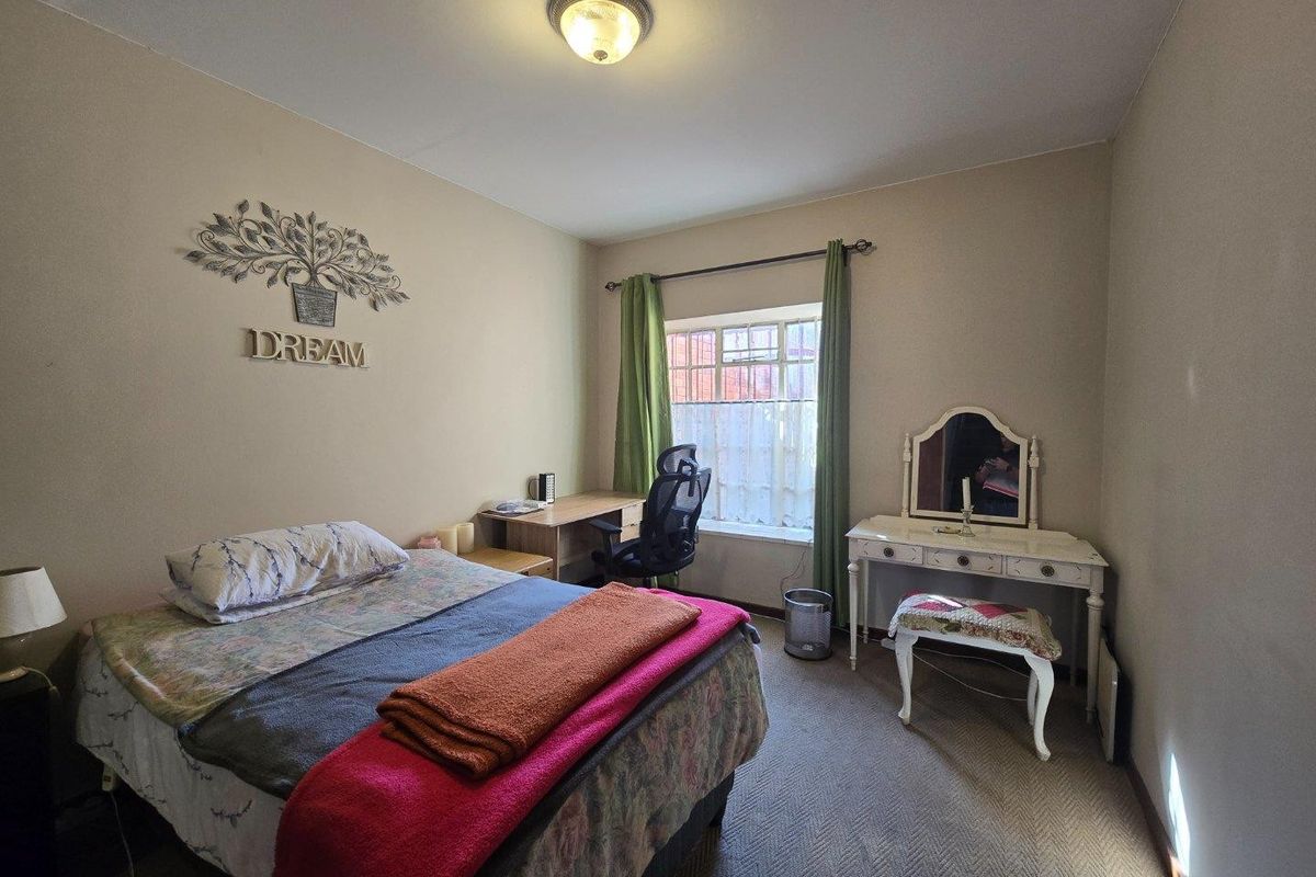 A standard bedroom featuring carpeted flooring, a central ceiling light fixture, and a window with an installed curtain rod.
