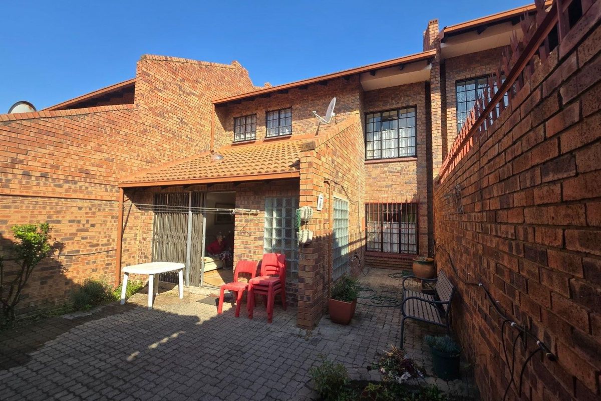Rear exterior view of a face brick townhouse featuring a paved courtyard, security gate, and glass block accents.