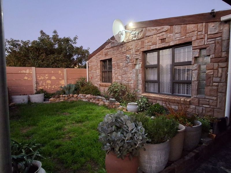 Rear garden area featuring a stone-clad exterior wall, security-fitted windows, and a precast concrete boundary wall with some visible paint wear.