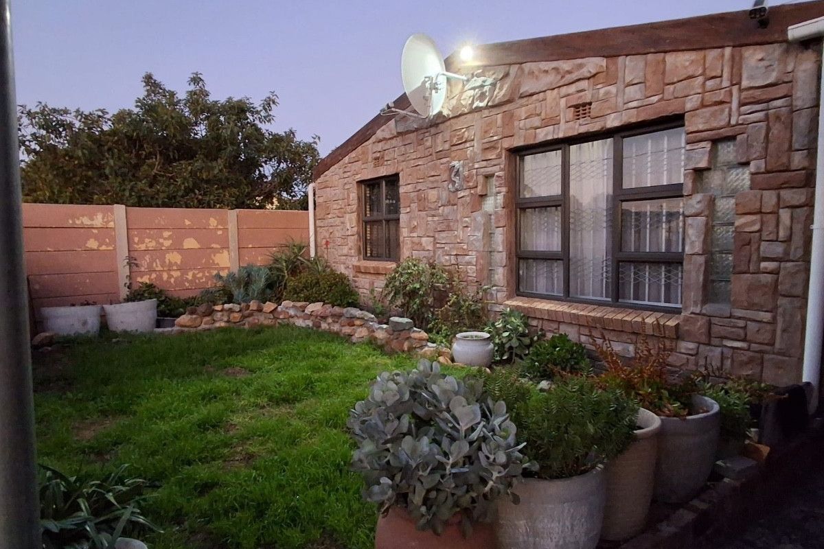 Rear garden area featuring a stone-clad exterior wall, security-fitted windows, and a precast concrete boundary wall with some visible paint wear.