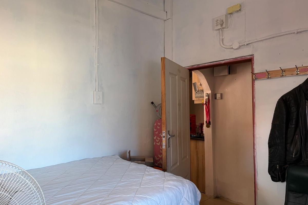 A bedroom featuring exposed electrical conduit and an arched doorway leading to an adjacent space, requiring cosmetic updates to improve the finish.