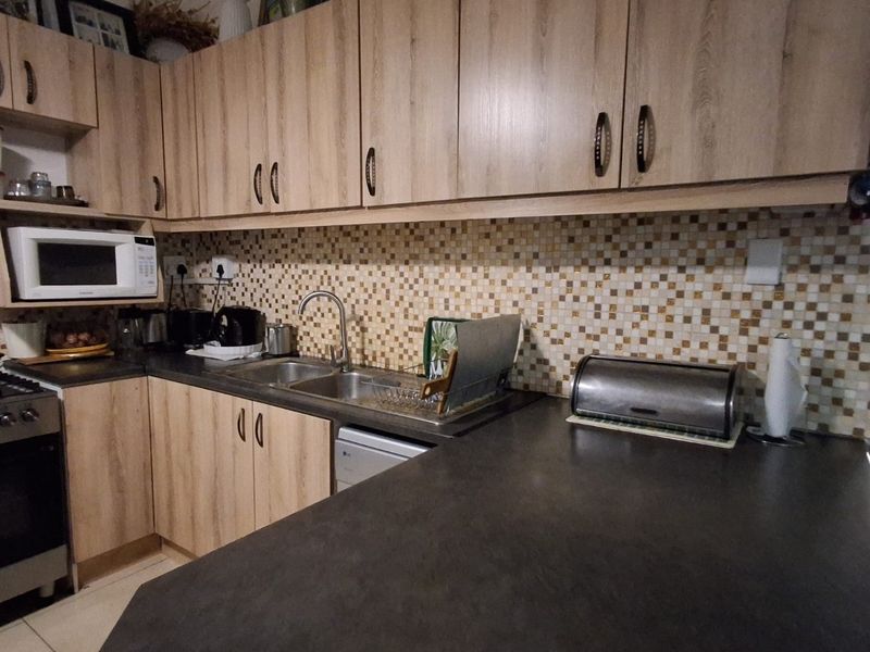 A functional kitchen featuring light wood-look cabinetry, a dark countertop, mosaic tile backsplash, and integrated appliances including a stove and microwave.