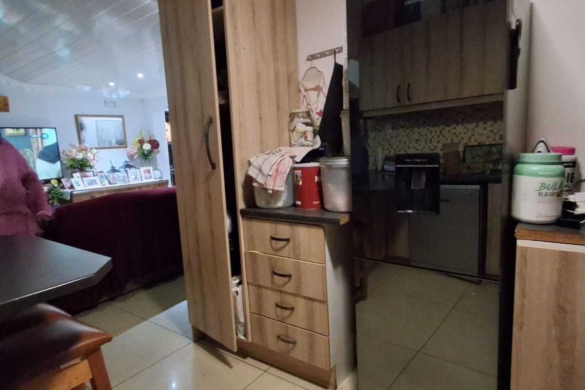 A functional kitchen area featuring built-in cabinetry, laminate countertops, and tiled flooring, with an open-plan layout connecting to the adjacent living space.
