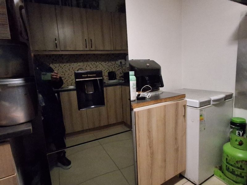 A functional kitchen area featuring wood-look cabinetry, tiled backsplash, and tiled flooring, providing essential storage and preparation space.