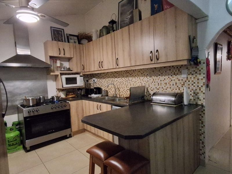A functional kitchen featuring light wood-finish cabinetry, a mosaic tile backsplash, a breakfast bar, and a stainless steel gas stove with an extractor fan.