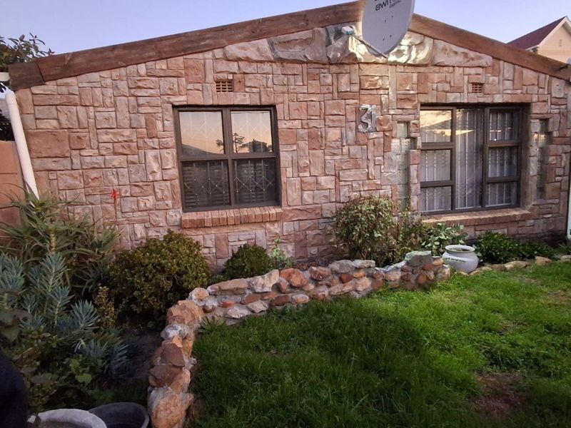 Front elevation of a house featuring stone cladding, security bars on windows, and a stone-bordered garden area.