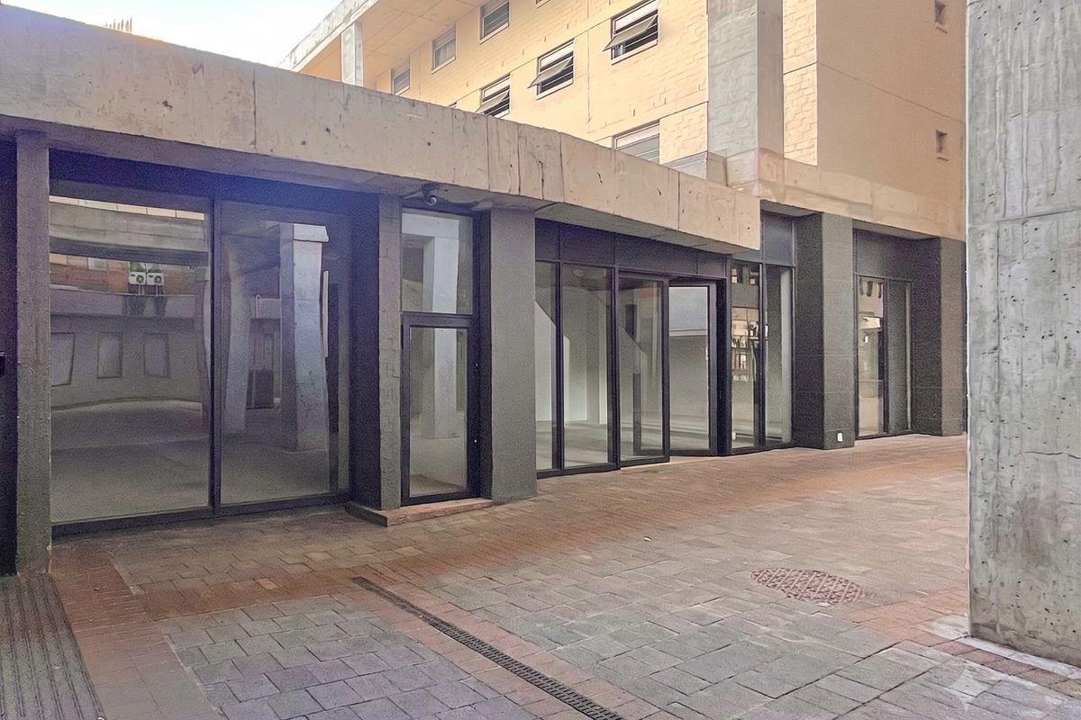 A modern retail storefront featuring large glass windows and a concrete facade, situated along a paved pedestrian walkway.
