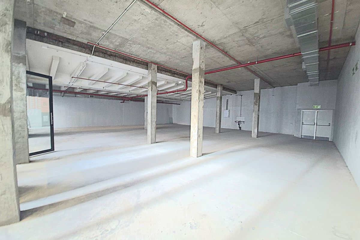 A large, open-plan retail shell featuring exposed concrete ceilings, support columns, and industrial fire safety infrastructure, ready for custom fit-out.
