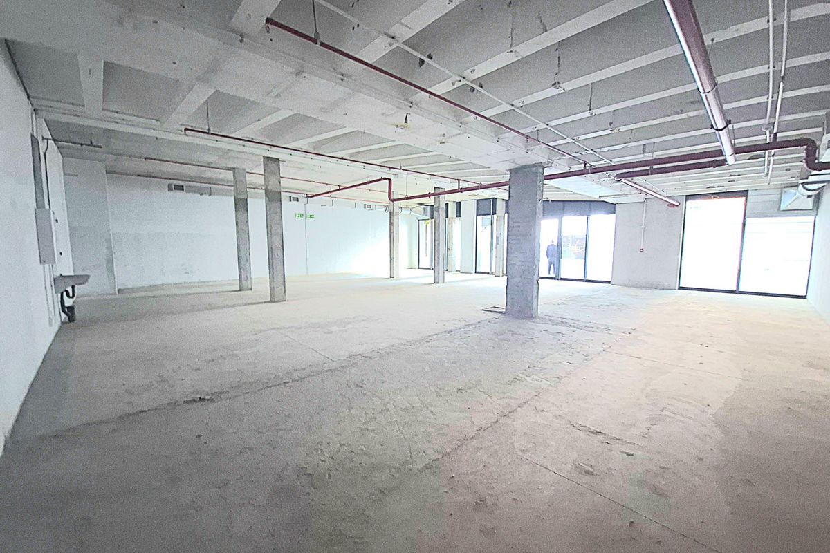 Spacious open-plan retail unit featuring an industrial aesthetic with exposed concrete ceilings, support columns, and large glass storefront windows.