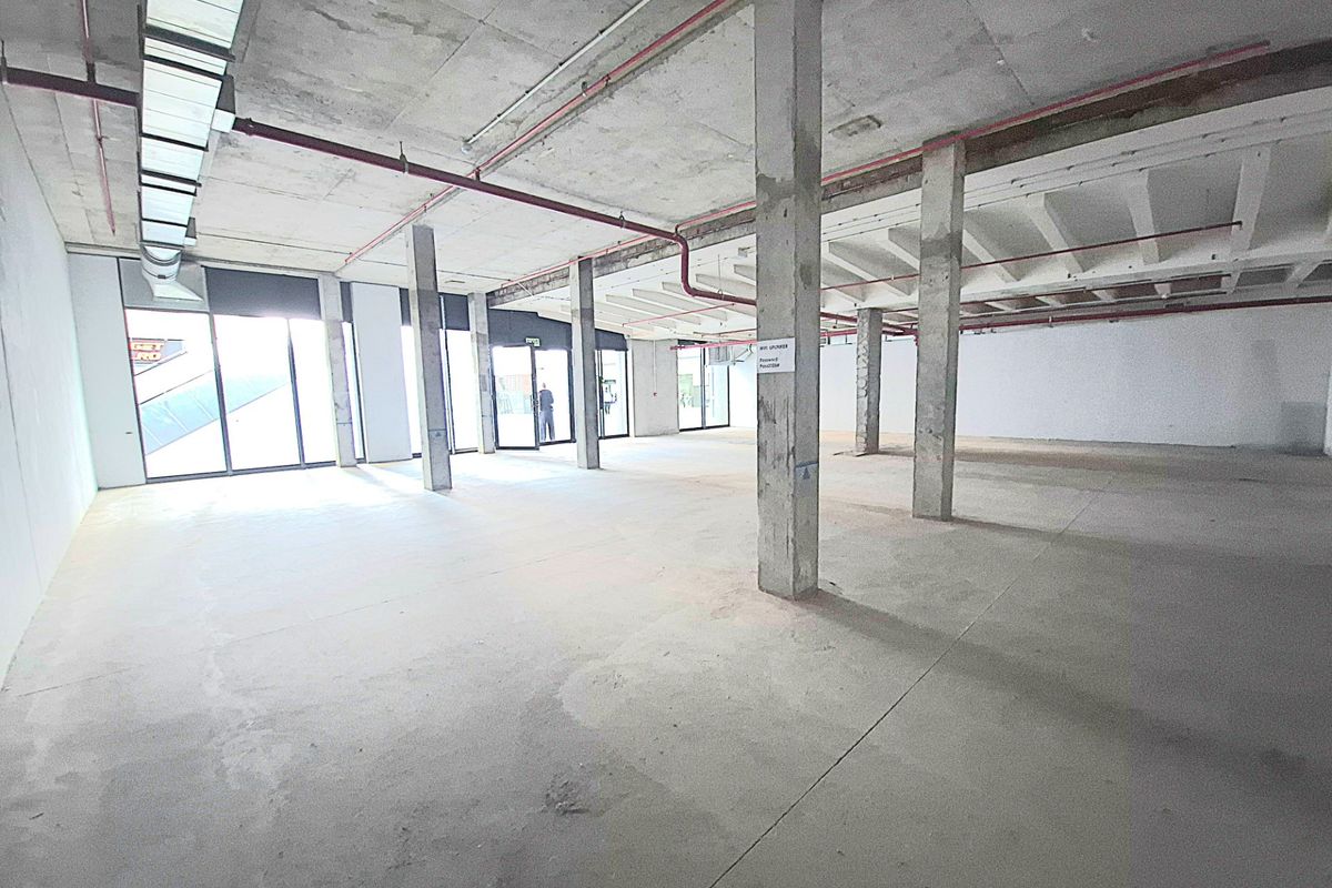 A large, open-plan retail space featuring exposed concrete ceilings, structural columns, and expansive glass storefront windows, currently in a shell condition.