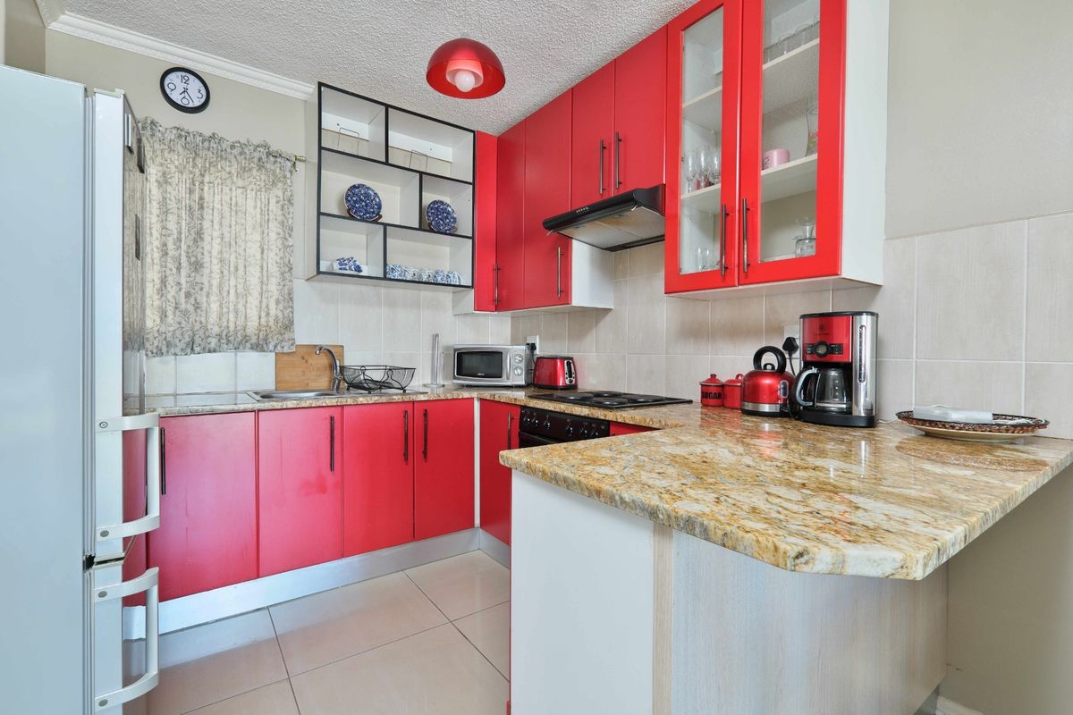 A functional kitchen featuring vibrant red cabinetry, granite countertops, a built-in oven and hob, and a tiled backsplash.