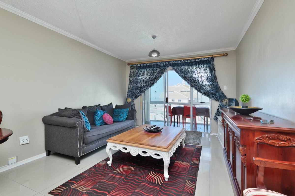 A comfortable living room featuring tiled flooring, coved ceilings, and a sliding glass door providing access to an outdoor balcony area.