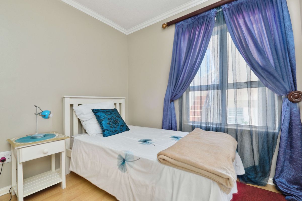 A compact bedroom featuring laminate flooring, neutral wall tones, and a window with decorative curtains.