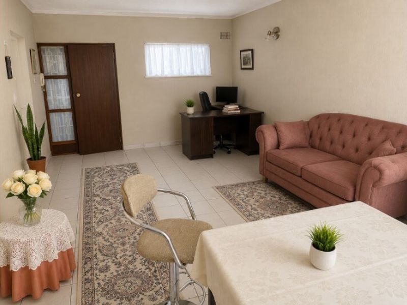 A spacious living area featuring neutral wall tones, tiled flooring, and a functional layout suitable for a combined lounge and home office setup.