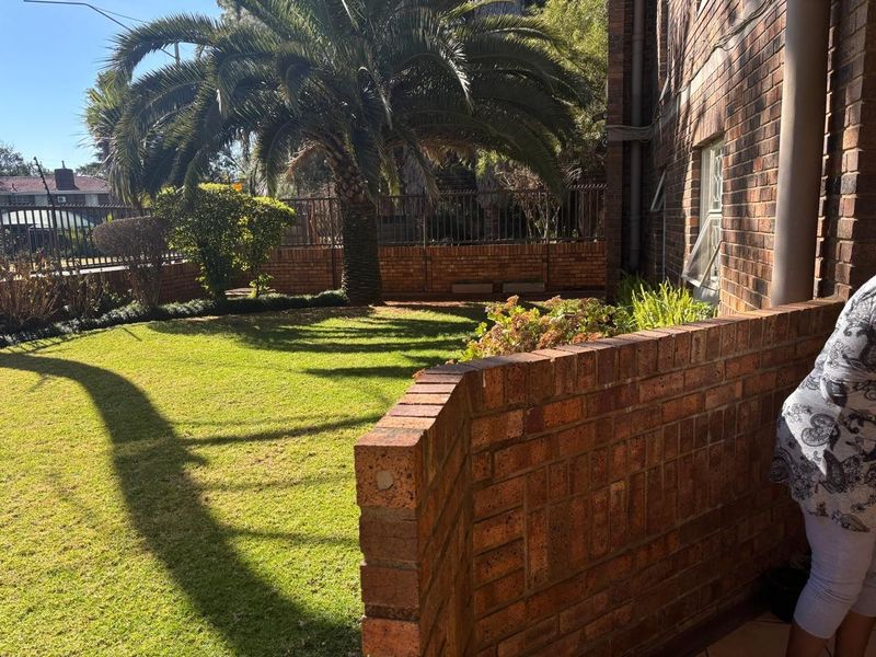 A view of the rear garden area featuring a well-maintained lawn, face brick exterior walls, and a perimeter boundary wall.