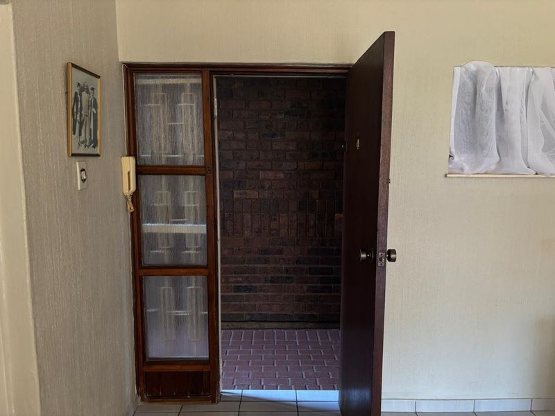An apartment entrance featuring a timber door, intercom system, and brickwork detail, leading to an outdoor tiled area.