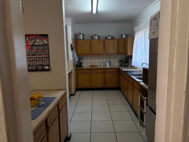 A functional kitchen featuring wooden cabinetry, tiled flooring, and a double basin sink with a tiled backsplash.