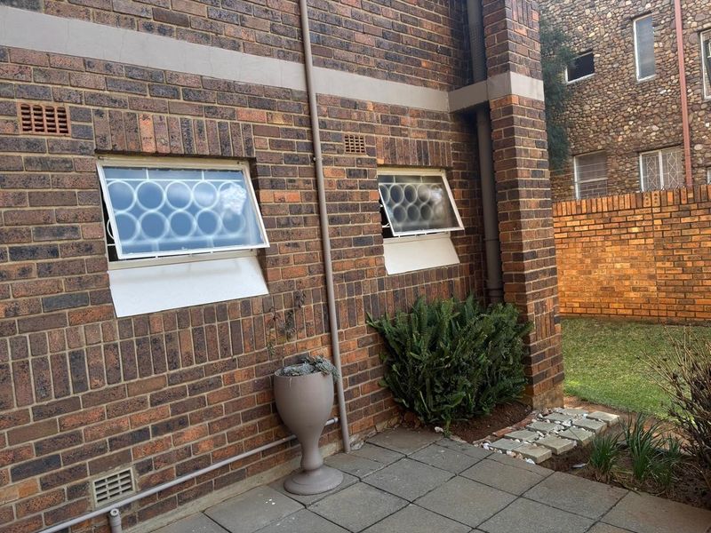 Rear exterior view of the apartment featuring a brick facade, paved patio area, and security-fitted awning windows.