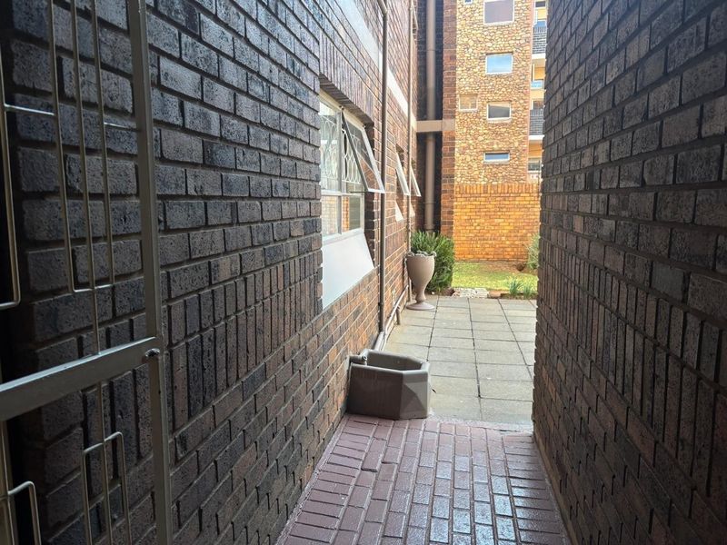 A narrow paved side passage leading to a rear courtyard area, featuring brick exterior walls and security window fixtures.