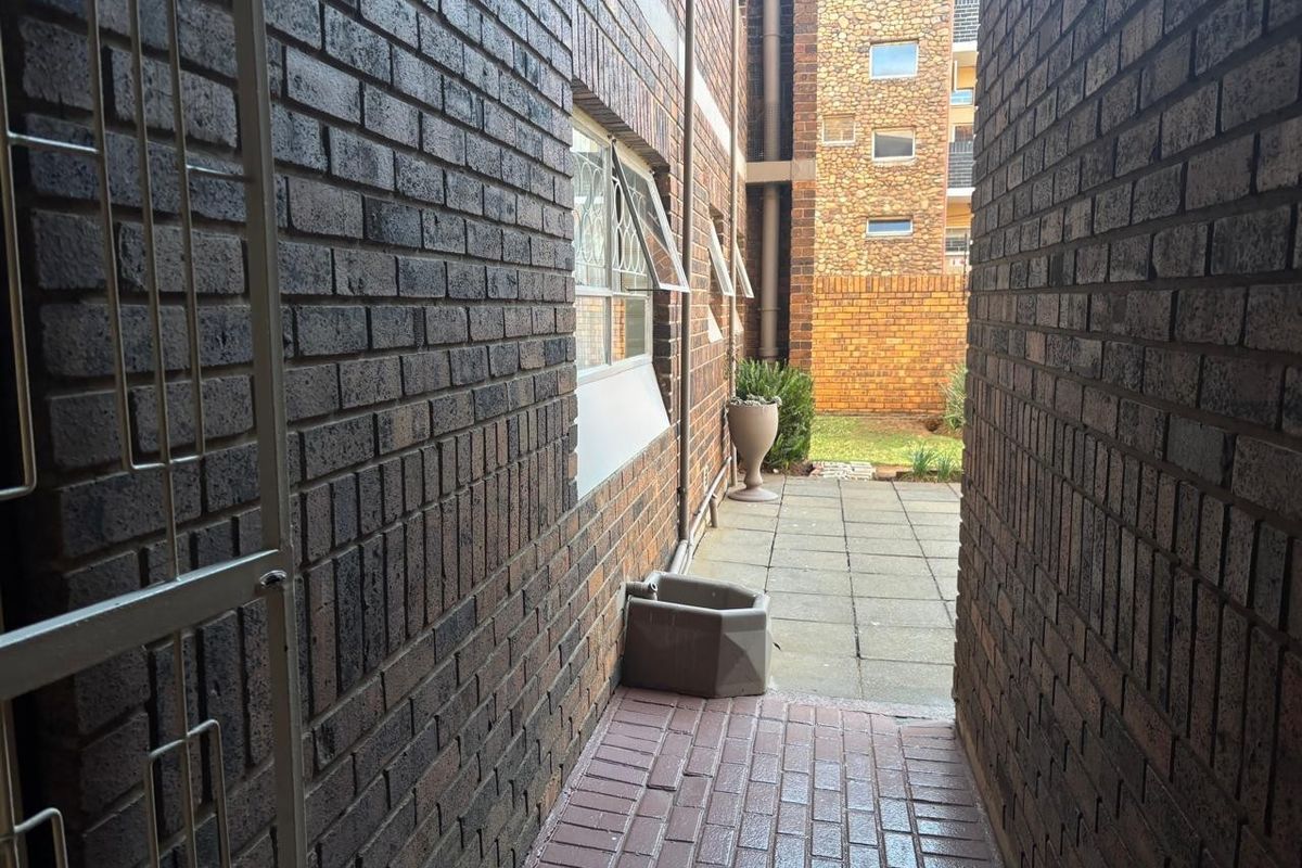 A narrow paved side passage leading to a rear courtyard area, featuring brick exterior walls and security window fixtures.