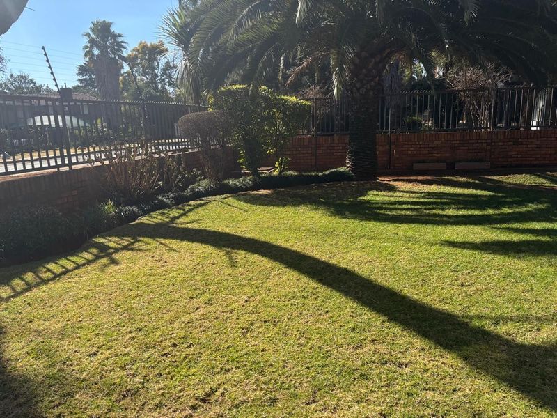 A private garden area featuring a well-maintained lawn, enclosed by brick boundary walls and secure metal fencing with integrated electric security wires.