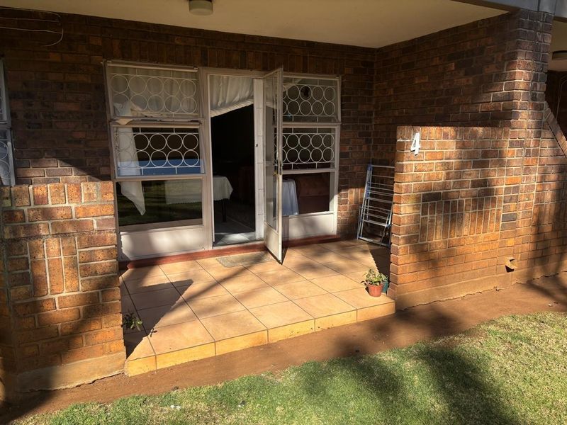 A ground floor patio area featuring exposed brick walls, tiled flooring, and a security gate entrance leading into the apartment.