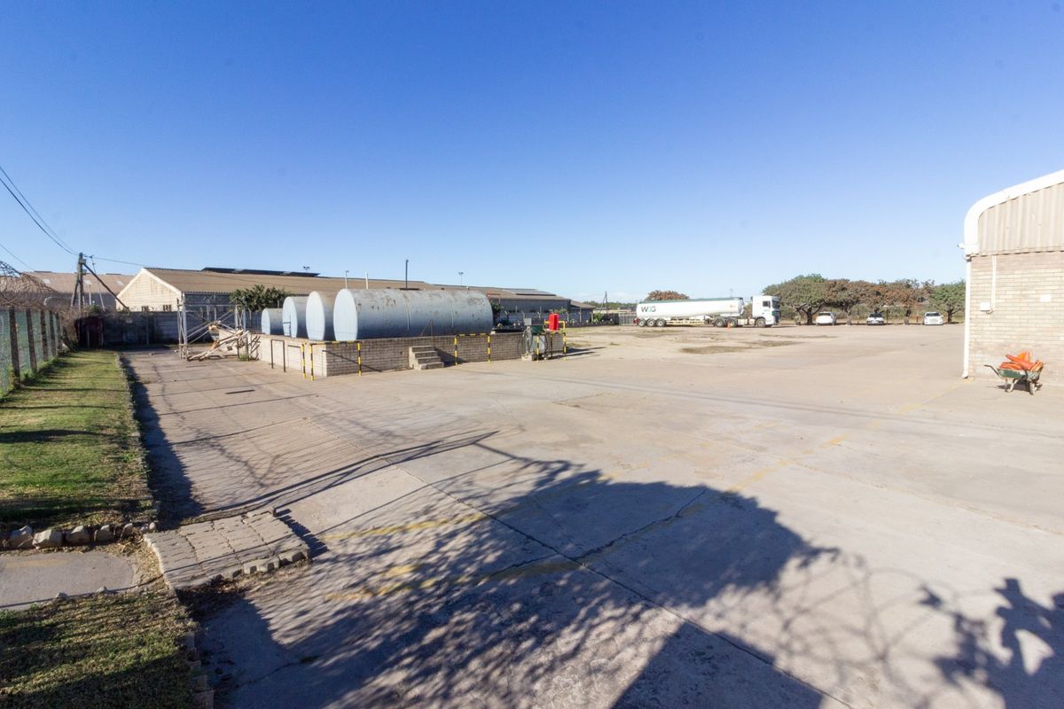 Expansive industrial yard featuring a concrete surface, large storage tanks on a raised brick platform, and perimeter fencing, suitable for heavy vehicle access.