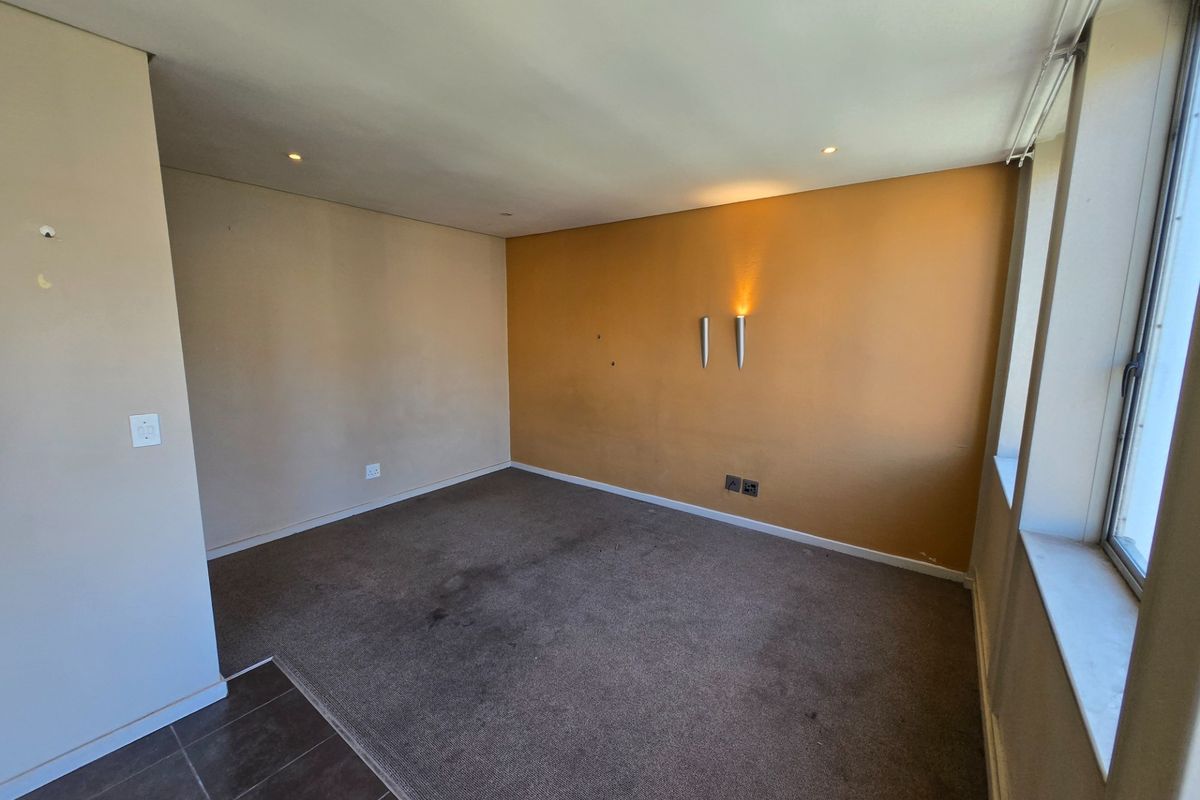 An empty bedroom featuring carpeted flooring, recessed downlights, and wall-mounted accent lighting, requiring cosmetic updates to the walls and flooring.