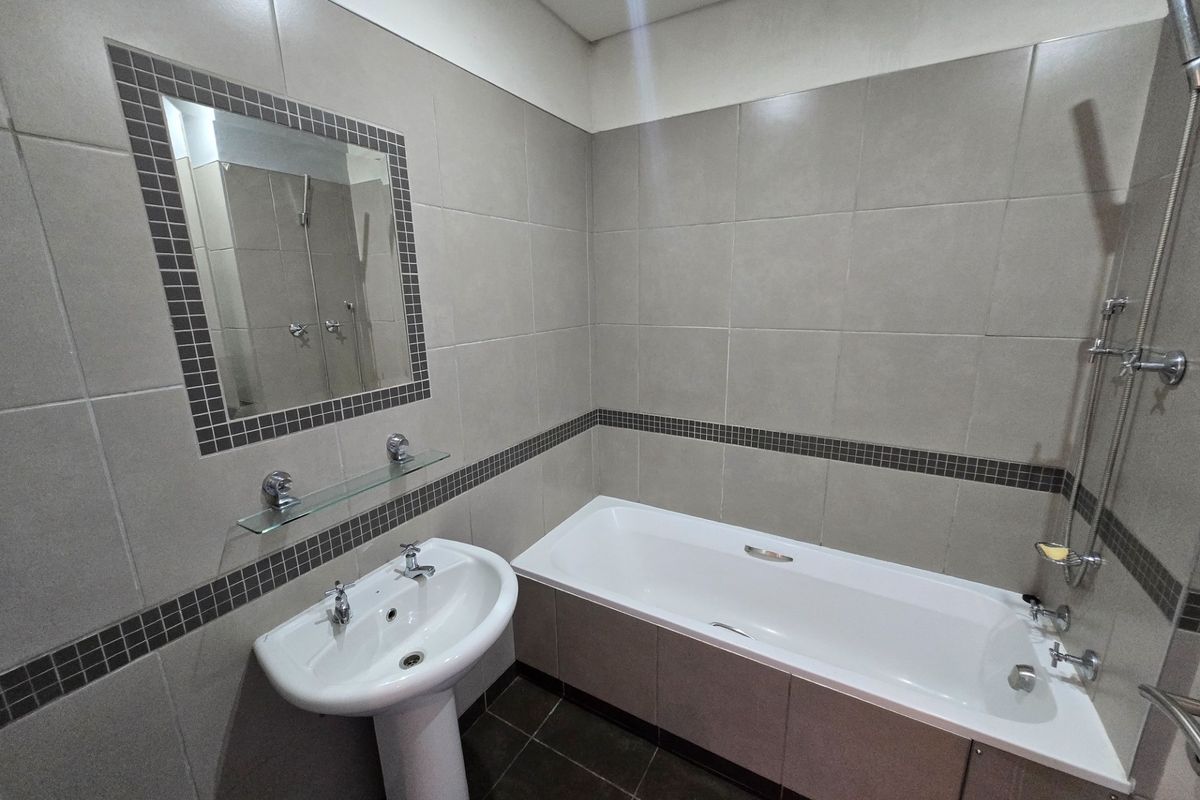 A clean, modern bathroom featuring a pedestal basin, a built-in bathtub with shower mixer, and neutral tiled finishes throughout.