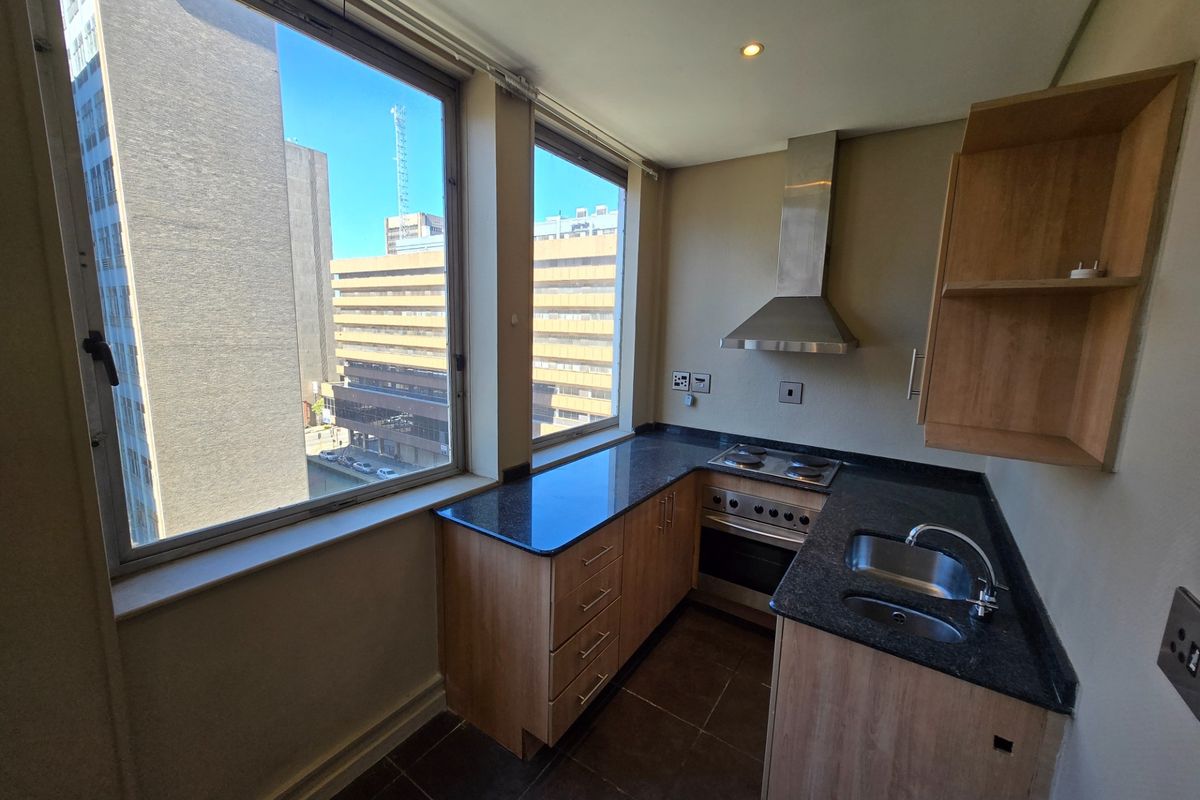 Compact kitchen featuring granite countertops, built-in oven, electric hob, stainless steel extractor fan, and ample cabinetry, with large windows offering urban views.