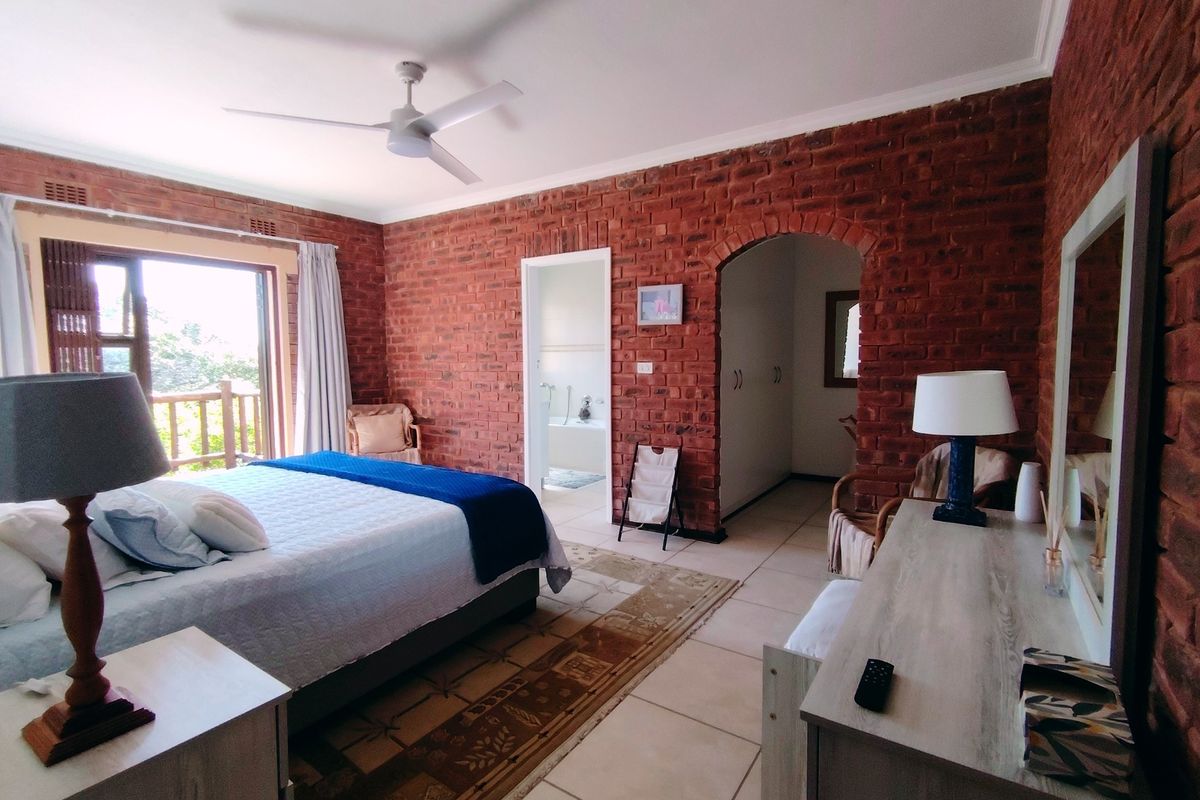 Spacious bedroom featuring exposed brick walls, tiled flooring, a ceiling fan, and direct access to a private balcony through sliding glass doors.
