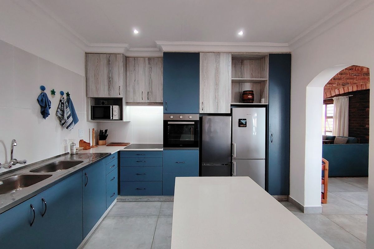 Modern kitchen featuring blue and wood-grain cabinetry, stone countertops, integrated oven, and a central island, with tiled flooring and recessed lighting.
