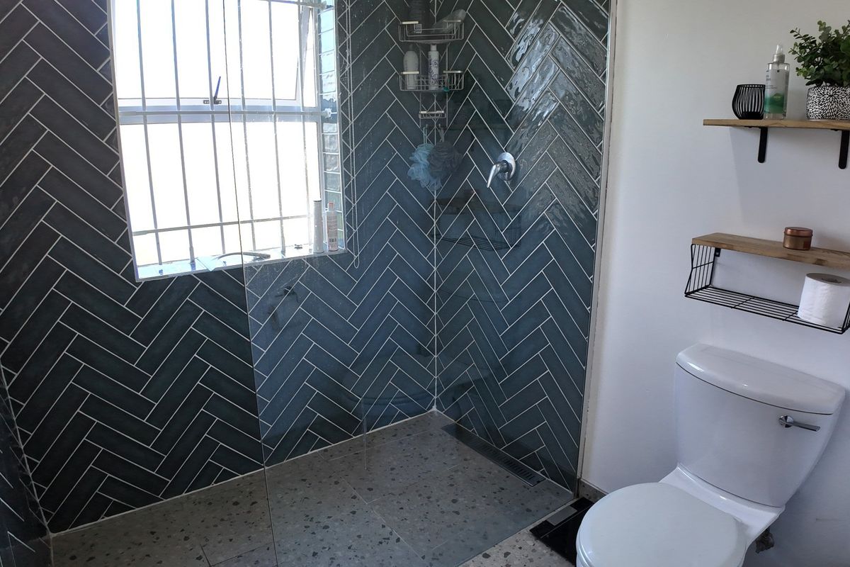 Modern bathroom featuring a walk-in shower with dark herringbone wall tiles, terrazzo flooring, and a white toilet.