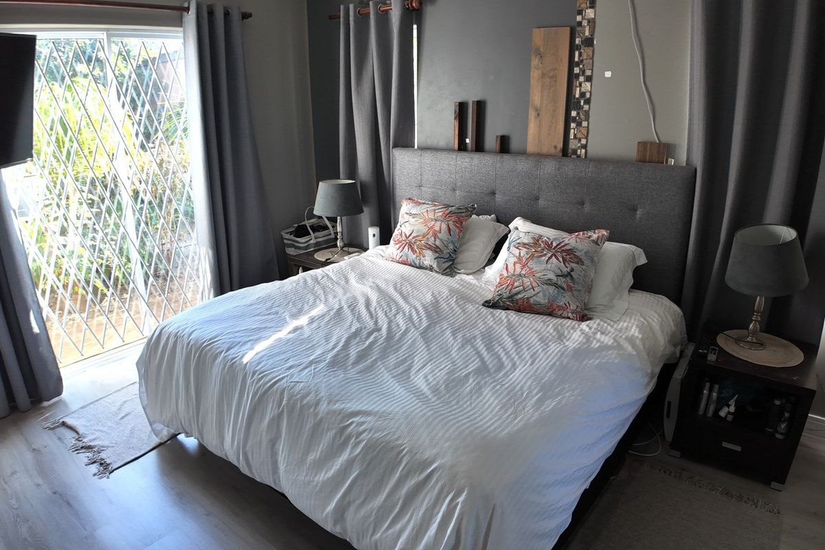 A well-lit bedroom featuring laminate flooring and a sliding glass door with security gate, providing direct access to the exterior.
