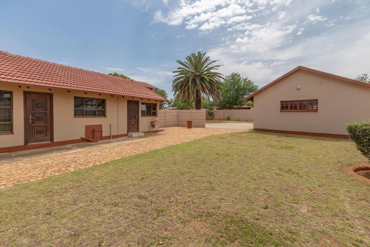 A view of the rear exterior featuring a paved driveway, lawn area, and separate outbuilding under a tiled roof.