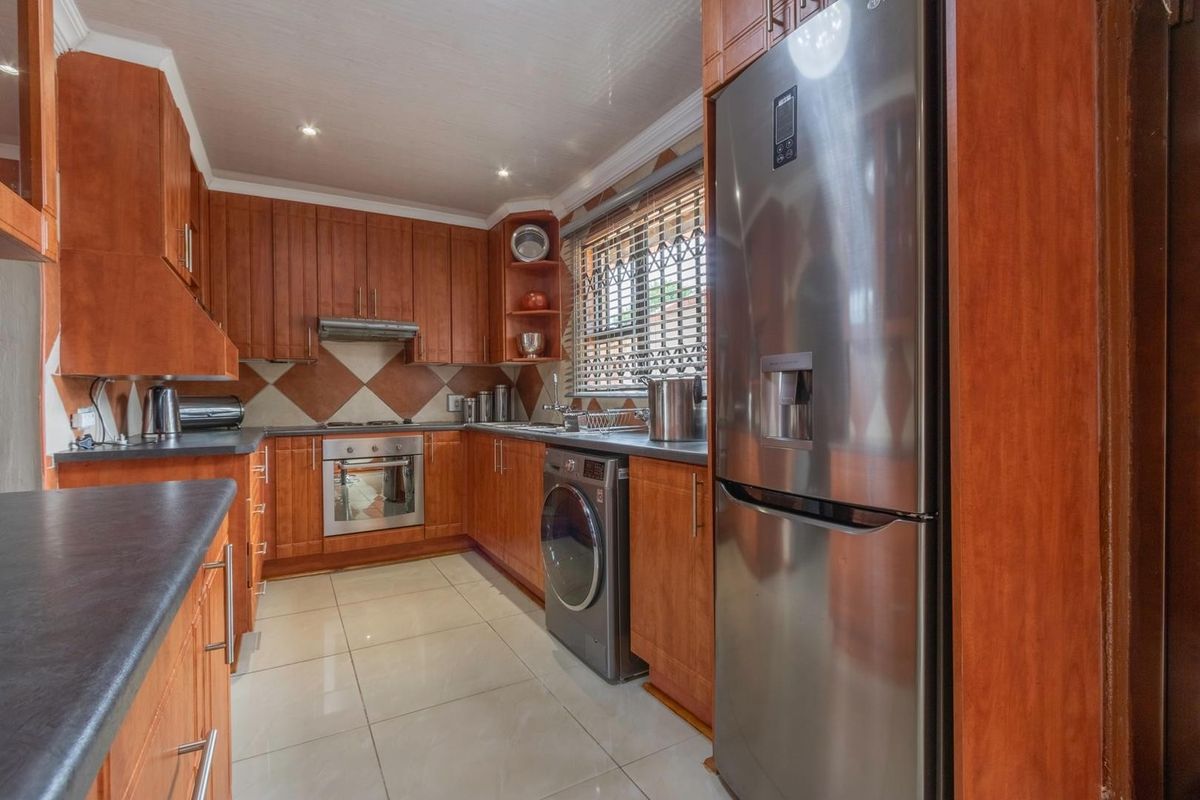 A functional kitchen featuring warm-toned wooden cabinetry, dark laminate countertops, tiled backsplash, and integrated appliances with tiled flooring throughout.