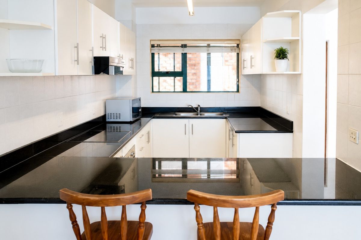 A well-maintained kitchen featuring white cabinetry, black granite countertops, a built-in hob, and a stainless steel sink with a tiled backsplash.