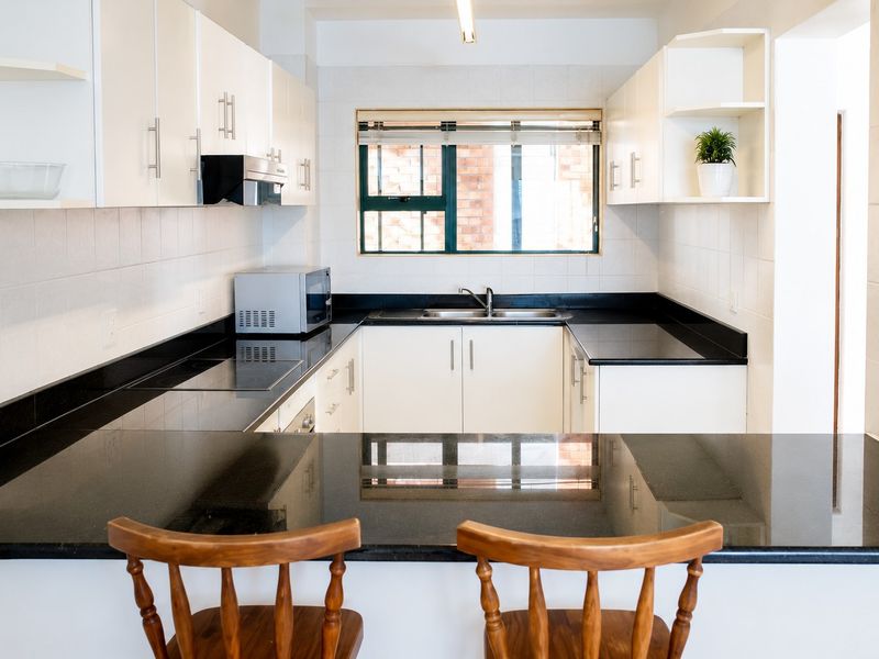 A well-maintained kitchen featuring white cabinetry, black granite countertops, a built-in hob, and a stainless steel sink with a tiled backsplash.